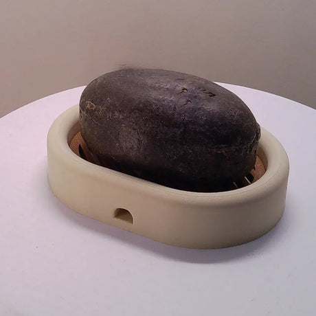 3D-printed oval soap dish with drain rack, white and wood-look.